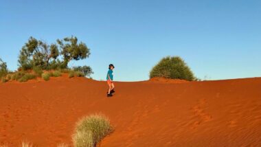 A little kid walking on dark red sand under a blue sky