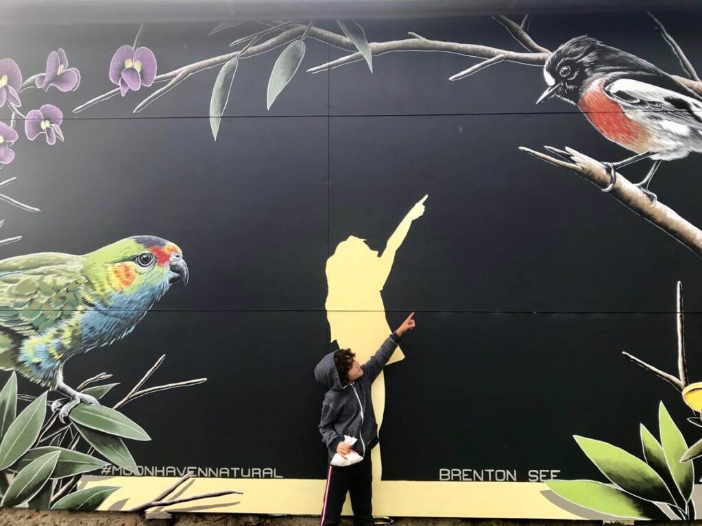 A toddler posing in front of a painted wall with birds