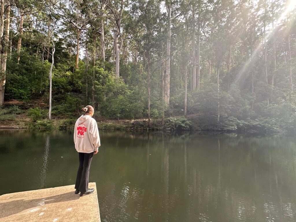A girl looking into Pemberton Pool which is surrounded by towering Karri trees with the sun gleaming through the gaps